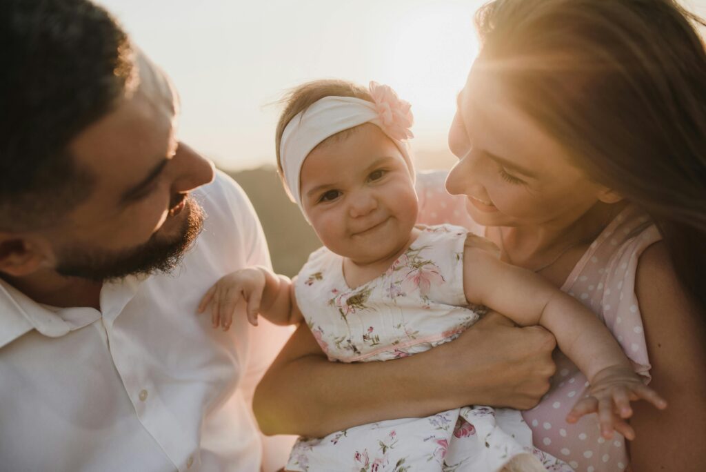 pexels-photo-5416619-5416619 A joyful family scene with parents holding their smiling baby at sunset.